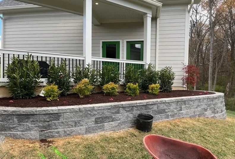 Morales Landscaping — stacked-stone retaining wall with mulched boxwood border at a residential front porch