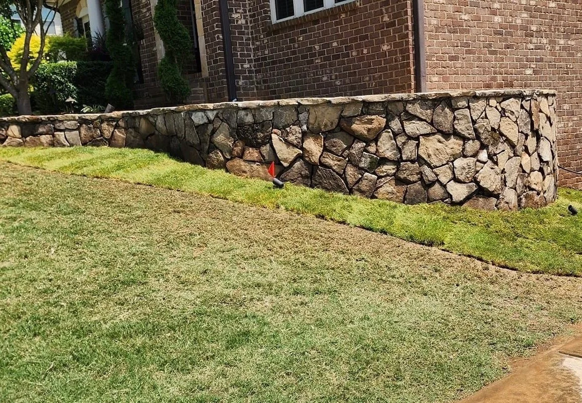 Morales Landscaping — natural stacked-stone retaining wall backing a freshly sodded front lawn along a brick home