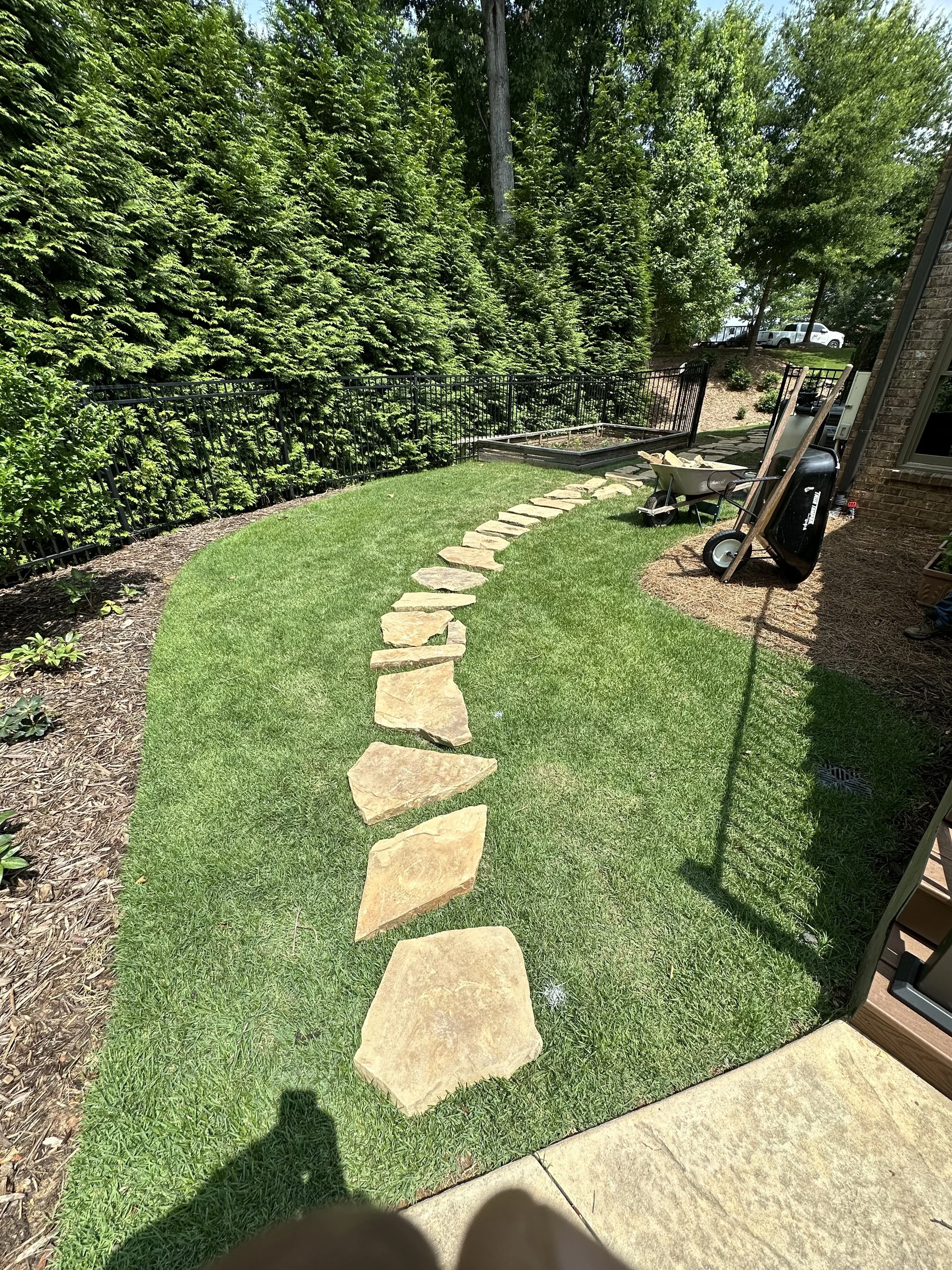 Morales Landscaping — curved flagstone stepping-path through a fresh-sodded backyard bordered by a privet hedge