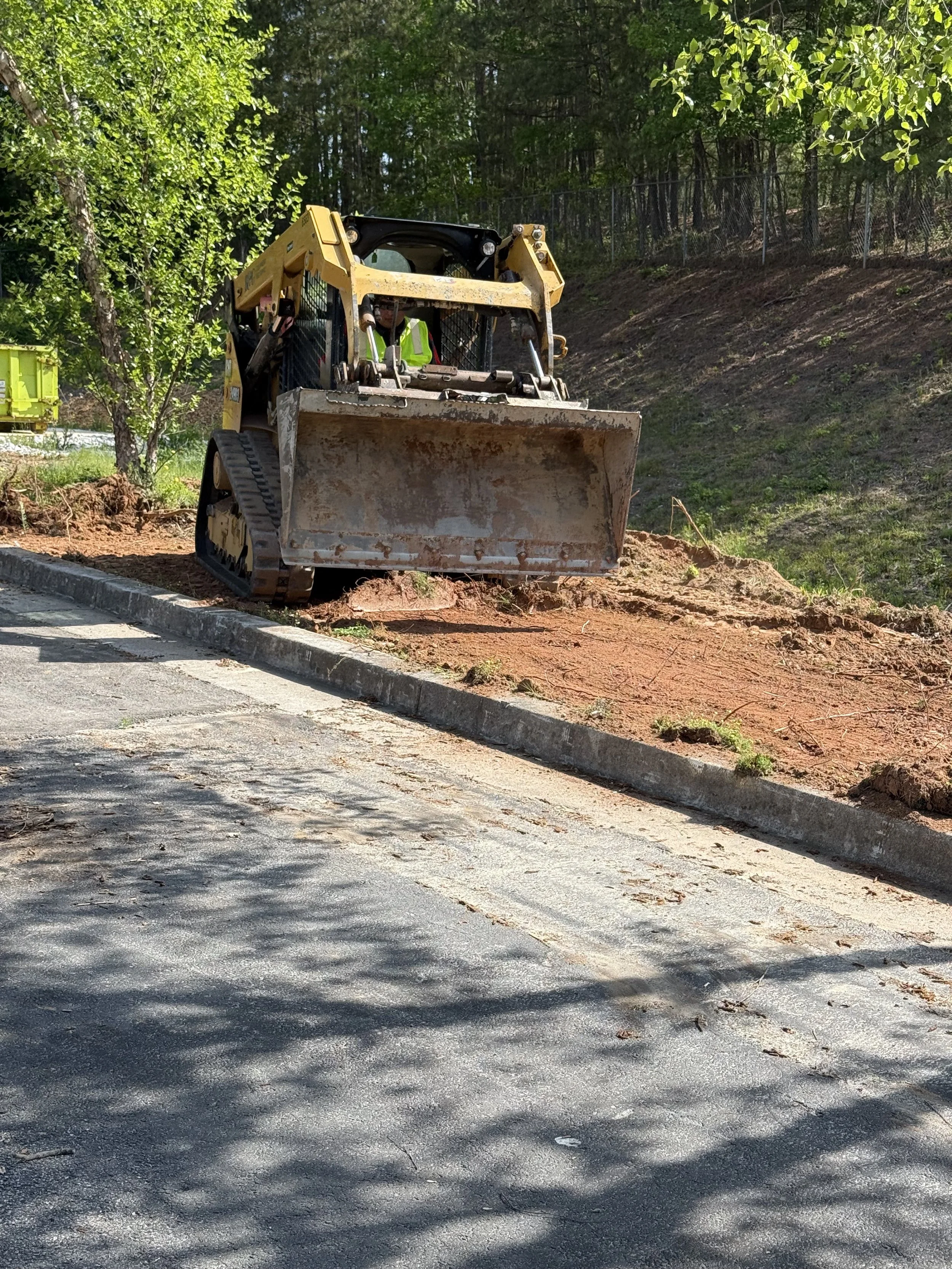 Morales Landscaping — Cat skid-steer loader grading a new curb-side bed with crew member operating